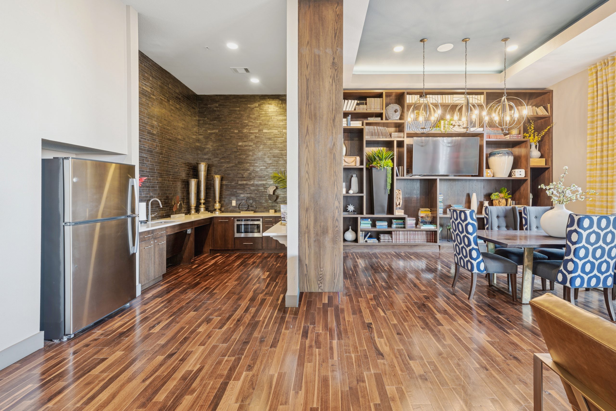 A full size kitchen, tv, bookshelves, and a table with blue chairs